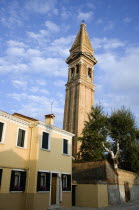 The leaning bell tower of the church on the lagoon island of Burano set behind colourful terraced housing Colorful