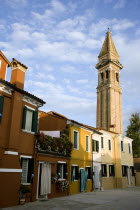 The leaning bell tower of the church on the lagoon island of Burano set behind colourful terraced housing Colorful