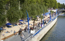 The Paris Plage urban beach. People strolling between the River Seine and other people lying on sand along the Voie Georges Pompidou usually a busy road now closed to traffic.