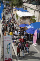 The Paris Plage city beach on the right bank of the River Seine where the road is closed and people lie in the sand and walk along the river bank. A sign in the foreground displays the attractions