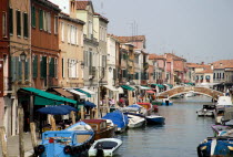 The main canal beside Fondamente dei Vetrai on Murano Island with boats moored at the quayside and a bridge across the canal