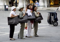 Asian tourists in St Marks Square posing for photographs whilst shouldering shopping bags from the nearby Gucci shop Store