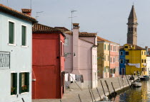 Colourful houses beside a canal on Burano. One of the few inhabited islands in the lagoon. The leaning tower of San Martino church in the distance Colorful