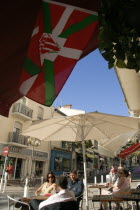 The Basque seaside resort on the Atlantic coast. The flag of Biarritz Rugby Football Club hanging up outside a bar with people sitting at tables under umbrellas
