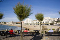The Basque seaside resort on the Atlantic coast. Tourists sitting on benches beneath tamarisk trees overlooking the Grande Plage beach with the Casino Municipal on the right.