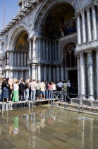 Aqua Alta High Water flooding in St Marks Square with tourists queuing on elevated walkways to enter St Marks Basilic