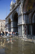 Aqua Alta High Water flooding in St Marks Square with tourists queuing on elevated walkways to enter St Marks Basilica