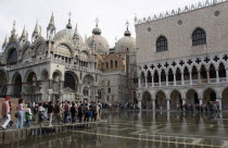 Aqua Alta High Water flooding in St Marks Square with tourists walking on elevated walkways above the water beside St Marks Basilica and the Doges Palac