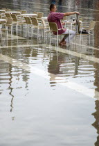 Aqua Alta High Water flooding in St Marks Square with an artist painting a watercolour seated at a table in the water of the flooded piazzaPaul Seheult