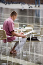 Aqua Alta High Water flooding in St Marks Square with an artist painting a watercolour seated at a table in the waterPaul Seheult