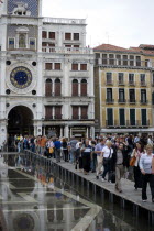 Aqua Alta High Water flooding in St Marks Square with tourists walking on elevated walkways beneath the Torre dellOrologio clock towerPaul Seheult