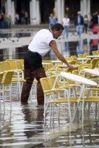 Aqua Alta High Water flooding in St Marks Square with waiter wearing waders and preparing restaurant tables