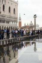 Aqua Alta High Water flooding in St Marks Square with tourists walking on elevated walkways outside the Doges Palace