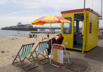 Lifegaurd station on The East Beach with Bournemouth Pier beyond tourists on the sandy beach and paddling in the sea.