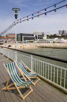 Deckchairs on the Pier withThe East Beach and the Imax Complex on the left beside seafront restaurants and bars. Adults and children play in the sand on the beach and at the waters edge between the gr...