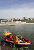 Speed Boat ride from the Pier with The East Beach and the Imax Complex on the left beside seafront restaurants and bars. Tourists enjoy the sandy beach.