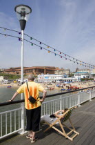 The Oceanarium and BICC Bournemouth International Conference Centre on the seafront seen from Bournemouth Pier with a watersports event taking place from the West Beach. Tourists on the pier.