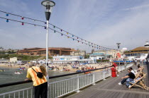 The Oceanarium and BICC Bournemouth International Conference Centre on the seafront seen from Bournemouth Pier with a watersports event taking place from the West Beach. Tourists on the pier.