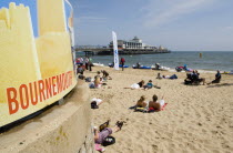 People lying on the beach on a sunny day with Bournemouth Pier in the background