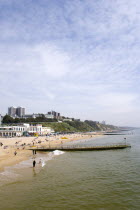 The East Beach showing the seafront attractions with people on the beach and at the waters edge between the groynes. Clifftop hotels and flats in the distance