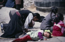 Pilgrims at Jokhang Monastery.  Kneeling woman and prostrate child on ground in front of temple entrance.