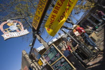 The Cowgirl Cafe outdoor eating area with customers and a waiter. Sign showing the days meals