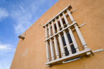 Wooden barred window on the side of an adobe style Pueblo Revival building