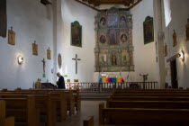The altar and nave of the San Miguel Mission church with a priest lighting candles beside the left wall