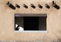 Detail of the Palace of The Governors in the Plaza with a man wearing a cowboy hat walking under the pueblo style arches