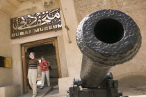 Entrance to the Museum with a cannon to one side and a couple walking through door.HolidaysTourismTravel Dubayy United Arab Emirates