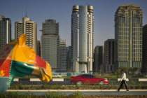 City centre skyline along the Corniche. Statue of a colourful patchwork camel  red car on road and a pedestrian.SkyscrapersModern ArchitectureTravelHolidaysTourismAutomobile Center United Arab E...