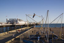Brighton Pier and amusements on the beach with people  bouncing on trampolines whilst suspended from harnesses on elastic ropes