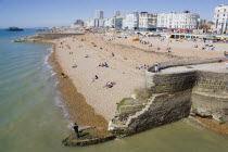 The beach and seafront with flint groyne in the foreground seen from Brighton Pier with the city in the distance