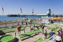 Tourist family playing crazy golf on the seafront with Brighton Pier beyond