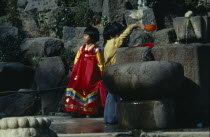 Children wearing traditional dress drinking from well.