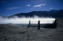 China, Tibet, Lhasa, Yangpachen geothermal powerstation with two women stood beside a pool of steaming water.