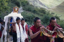 China, Tibet, Lhasa, Drak Yerpa Monastery complex. New statue being carried up to the monastery by monks led by trumpet blowers.