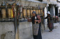 China, Tibet, Shigatse, Two elderly women spinning row of prayer wheels in the street.