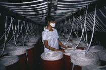 Woman surrounded by vats of yarn in textile factory.