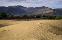 Wind rippled encroaching sand with mountain backdrop.