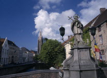 Religious statue on bridge over canal with church spire in distance Flemish Region