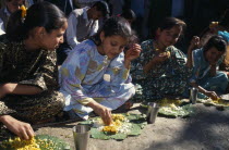 Girls eating from banana leaves with their hands at meal during country wedding.