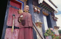 Lama holding prayer wheel outside monastery door.