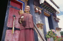 Lama holding prayer wheel outside monastery door.