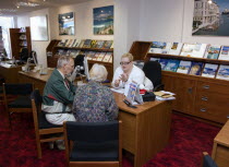 Male and female customer in a Travel Agents office discussing their holiday arrangements with a female travel consultantEuropean Great Britain Northern Europe UK United Kingdom British Isles