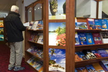 Male customer in a Travel Agents office looking through travel brochures displayed on shelvesEuropean Great Britain Northern Europe UK United Kingdom British Isles