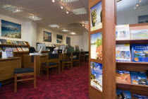 Male and female customer in a Travel Agents office discussing their holiday arrangements with a female travel consultant with travel brochures on shelves in the foregroundEuropean Great Britain North...