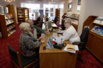 Male and female customer in a Travel Agents office discussing their holiday arrangements with a female travel consultantEuropean Great Britain Northern Europe UK United Kingdom British Isles