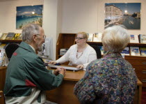 Male and female customer in a Travel Agents office discussing their holiday arrangements with a female travel consultantEuropean Great Britain Northern Europe UK United Kingdom British Isles