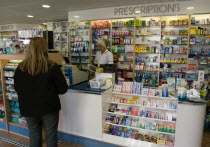 Interior of high street dispensing chemist  with female customer collecting her prescription from the pharmacist assistant standing behind the counterEuropean Great Britain Northern Europe UK United...